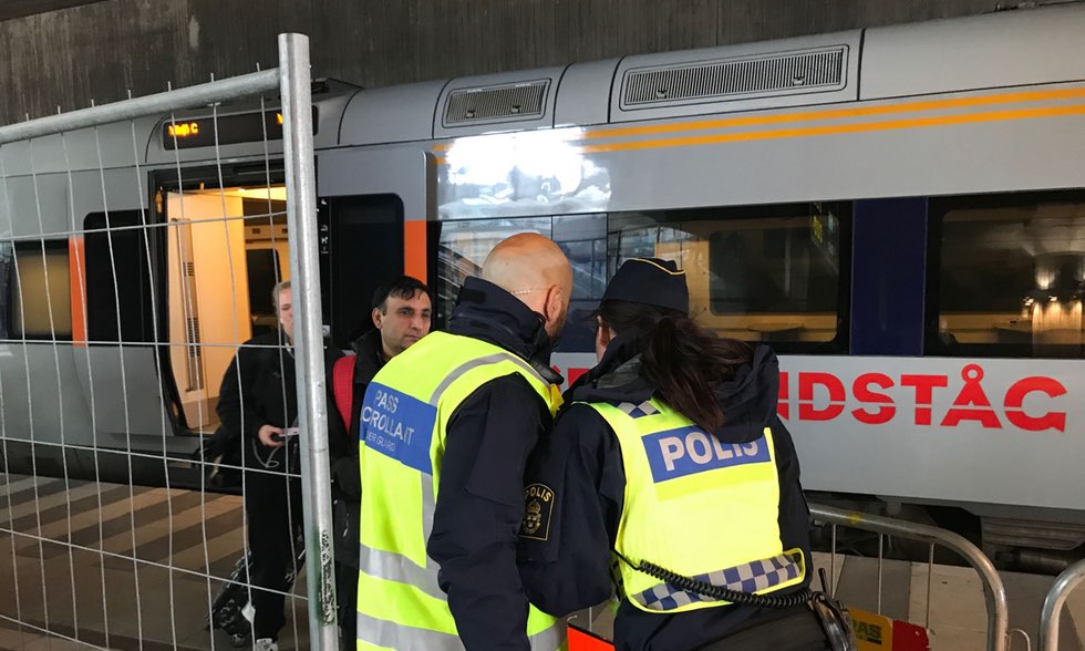 Två poliser i reflexväst står framför ett tåg och kollar en mans id.