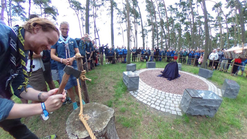 Scouter står i en ring och tittar på när Scouternas ordförande hugger av ett rep med en yxa.