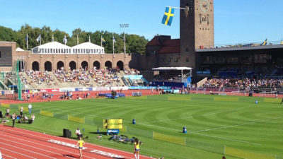 En stadio syns i solsken. På löparbanorna står några svenska idrottare.