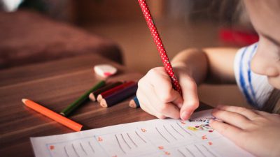 En flicka skriver med en röd penna på ett papper.