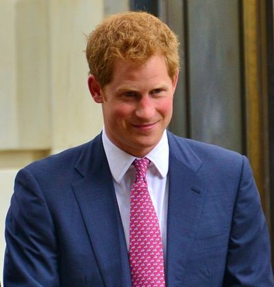 Prins Harry står i en blå kavaj och ser glad ut