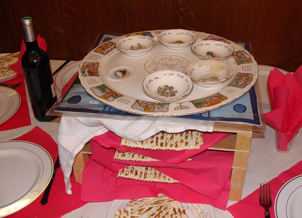 Ett bord med tallrikar. I mitten står en träställning med flera hyllor. På varje hylla ligger ett platt bröd. Överst står en tallrik med flera små skålar. Bredvid står en flaska med vin.