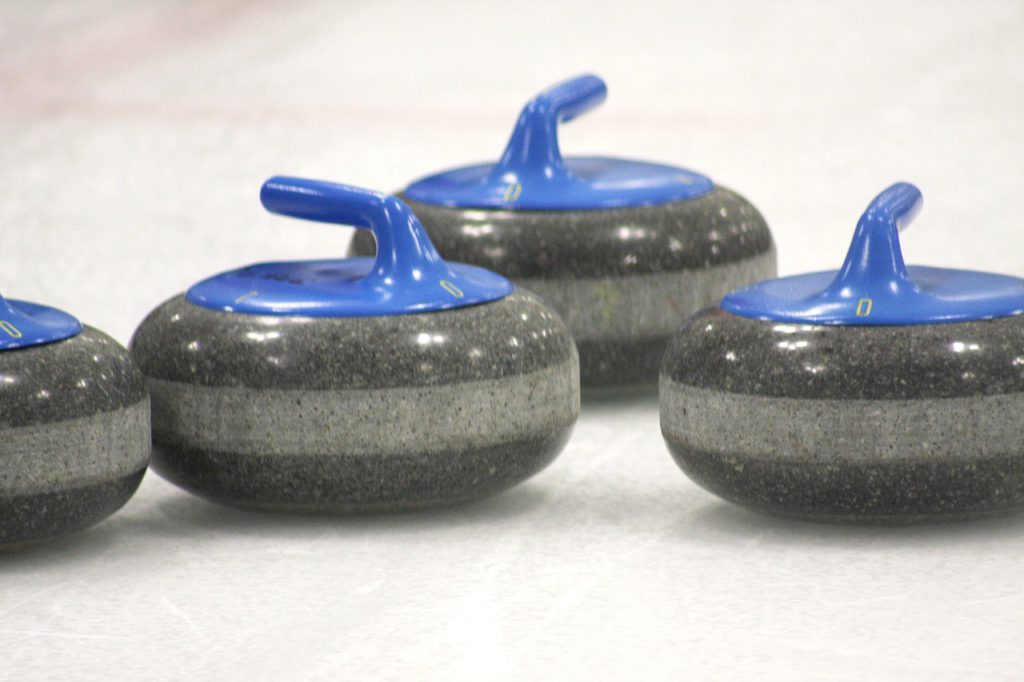 Grå curlingstenar med blå handtag som ligger på is