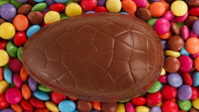 Ett stort chokladägg ligger på en bädd av färgglada chokladlinser.