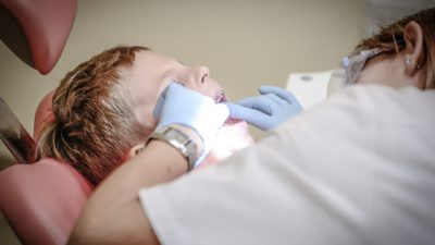 En pojke blir undersökt av en tandläkare med ljusblå handskar