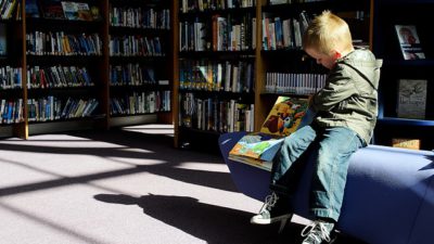 Ett barn sitter på ett bibliotek och bläddrar i en bok.