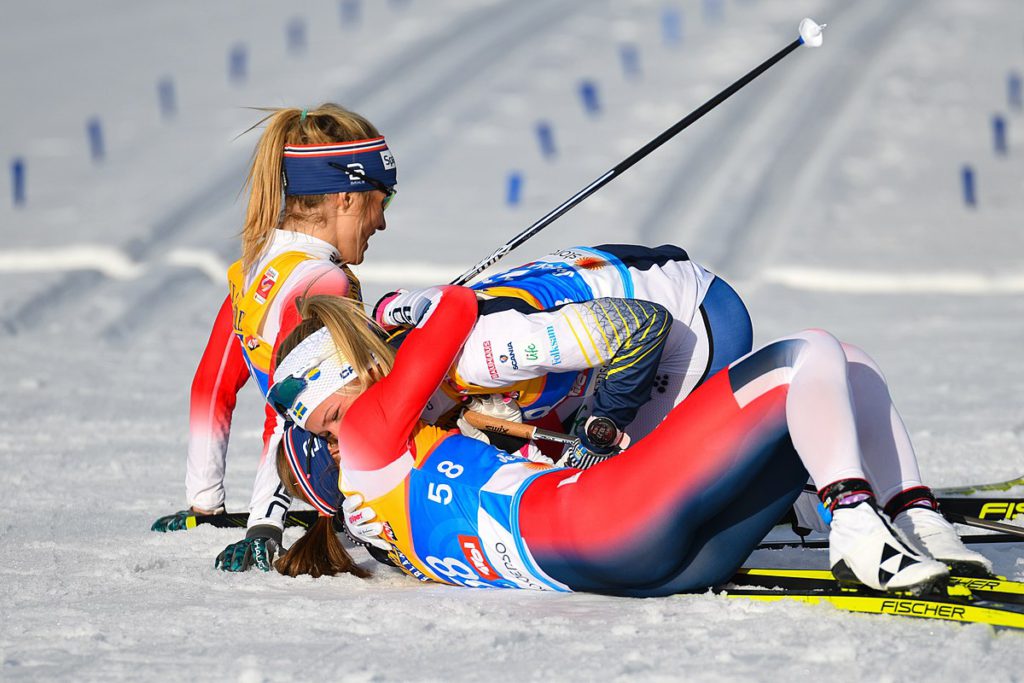 Frida Karlsson och två andra skidåkare ligger ner i snön och kramas efter att ha passerat mållinjen i skid-VM.