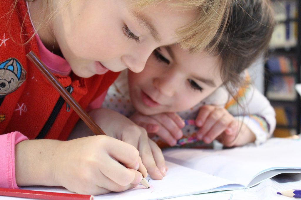 Två barn hjälper varandra med en klurig uppgift. Den ena skriver i ett skrivblock och den andra är nyfiken och intresserad.
