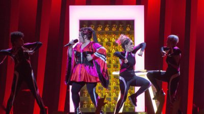 Bild från Eurovision 2018. På scenen syns artisten Netta med fyra dansare i bakgrunden. Hon håller i en mick och dansarna gör stora gester.