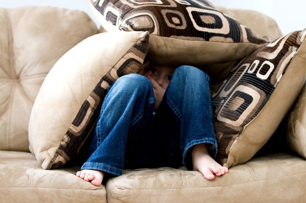 Ett barn gömmer sig under tre stora kuddar i en soffa.