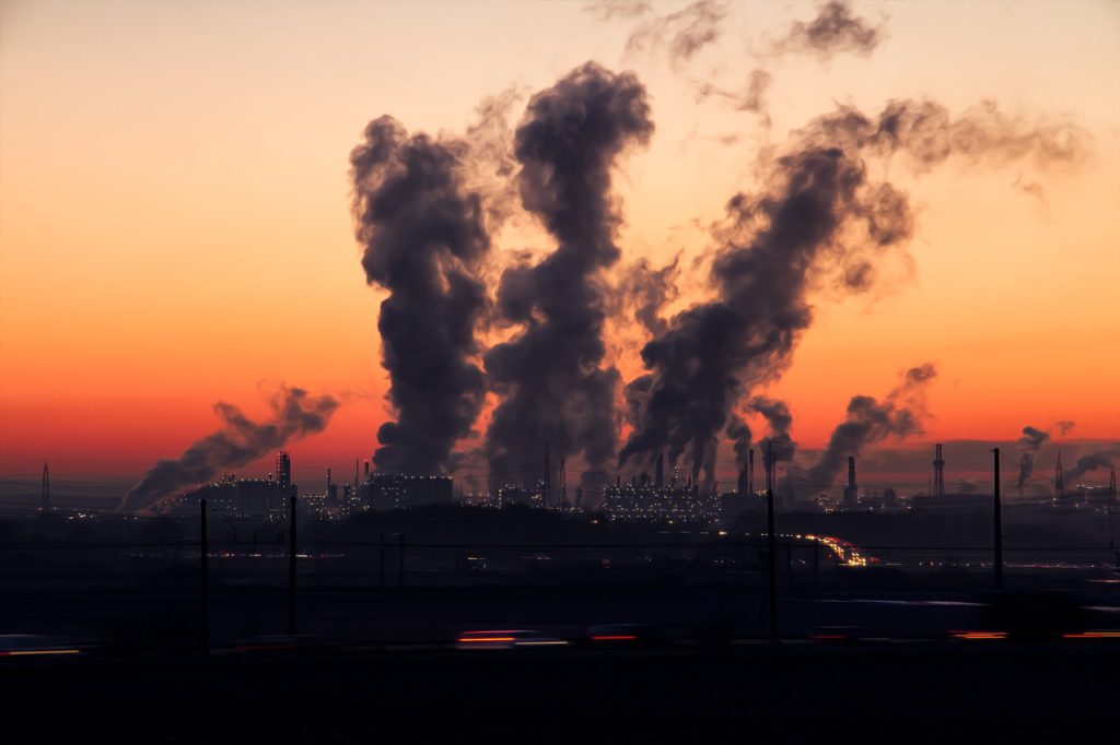 I solnedgången står det flera stora fabriker som släpper ut stora moln på himlen.
