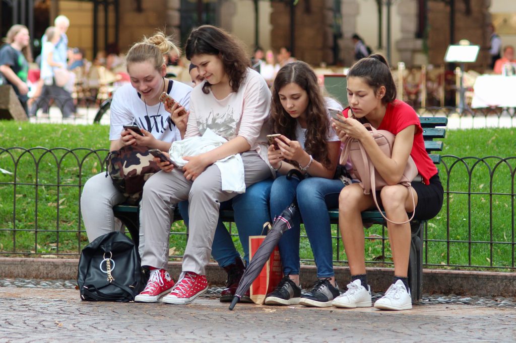 Unga tjejer som sitter på ett staket och använder sina mobiler