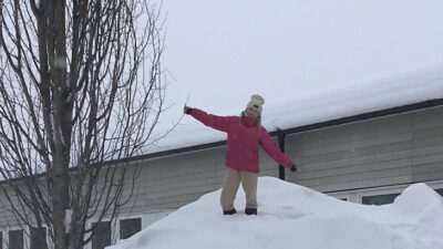 En elev i rosa jacka står högst upp på en stor snöhög.
