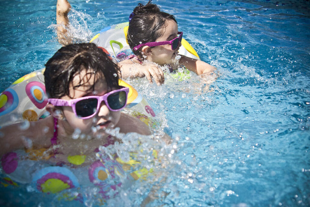 Två barn som badar med badringar och solglasögon.