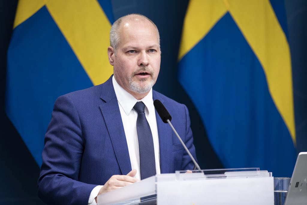 justitie- och inrikesministern Morgan Johansson håller ett tal framför två svenska flaggor.